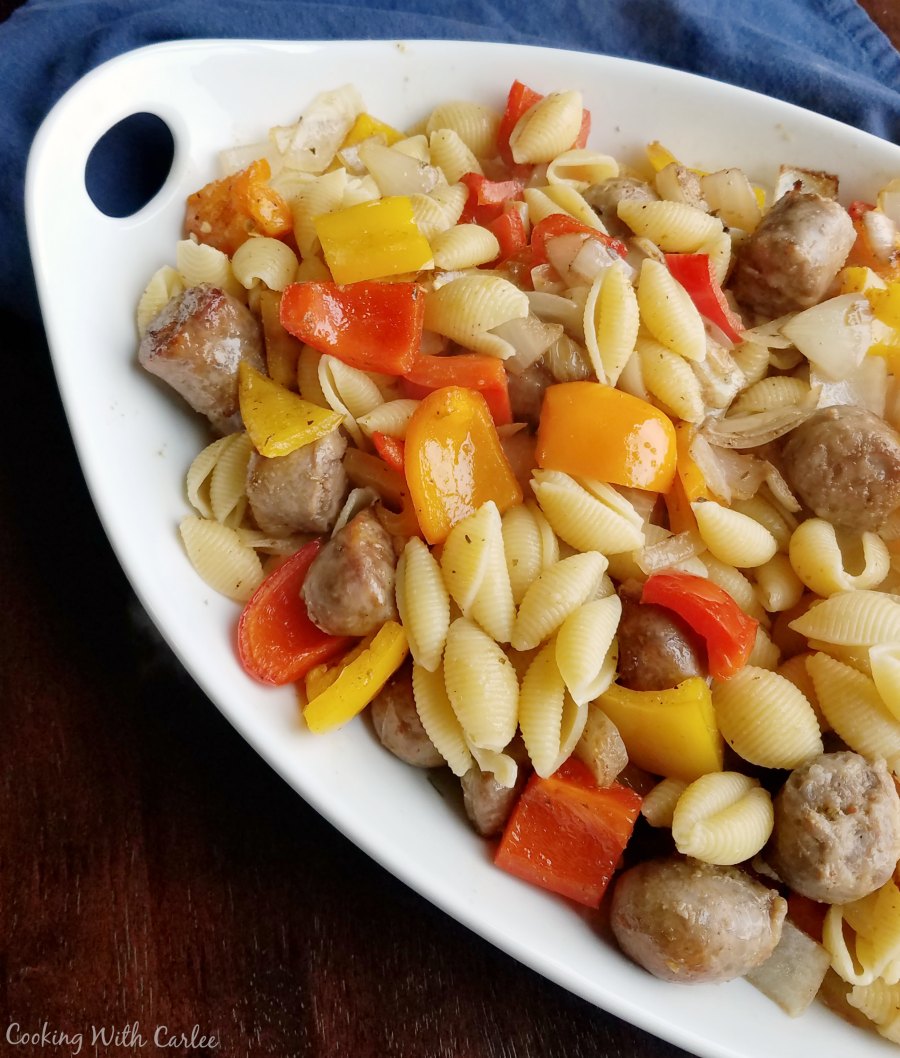 large serving dish filled with pasta tossed with sausage, peppers and onions.