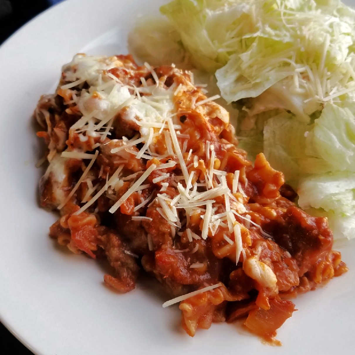 serving of skillet lasagna with shredded parmesan and salad on a plate.