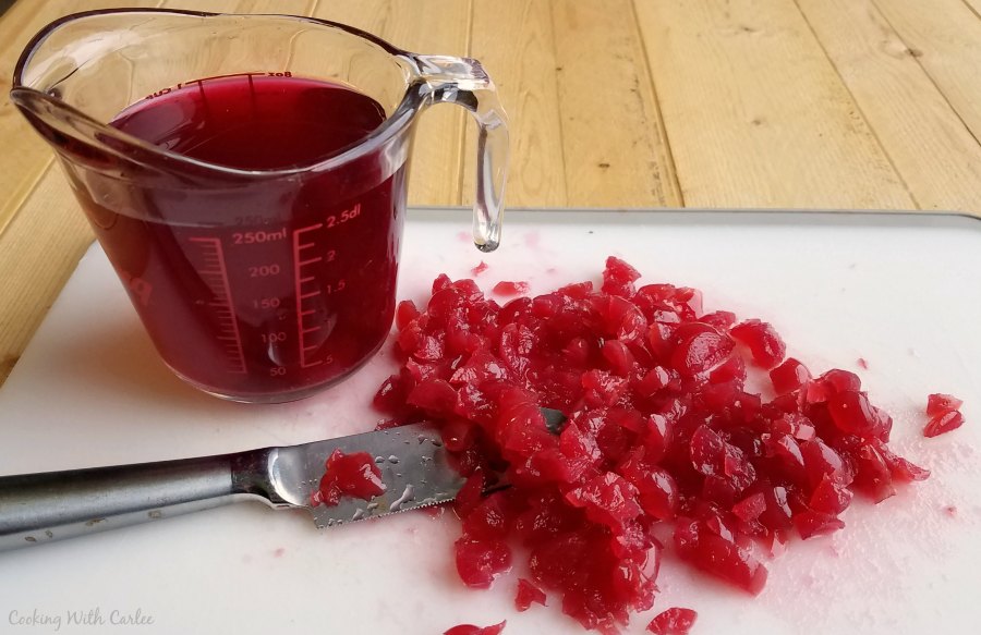 chopped cherries and knife on cutting board with measuring cup of cherry juice.