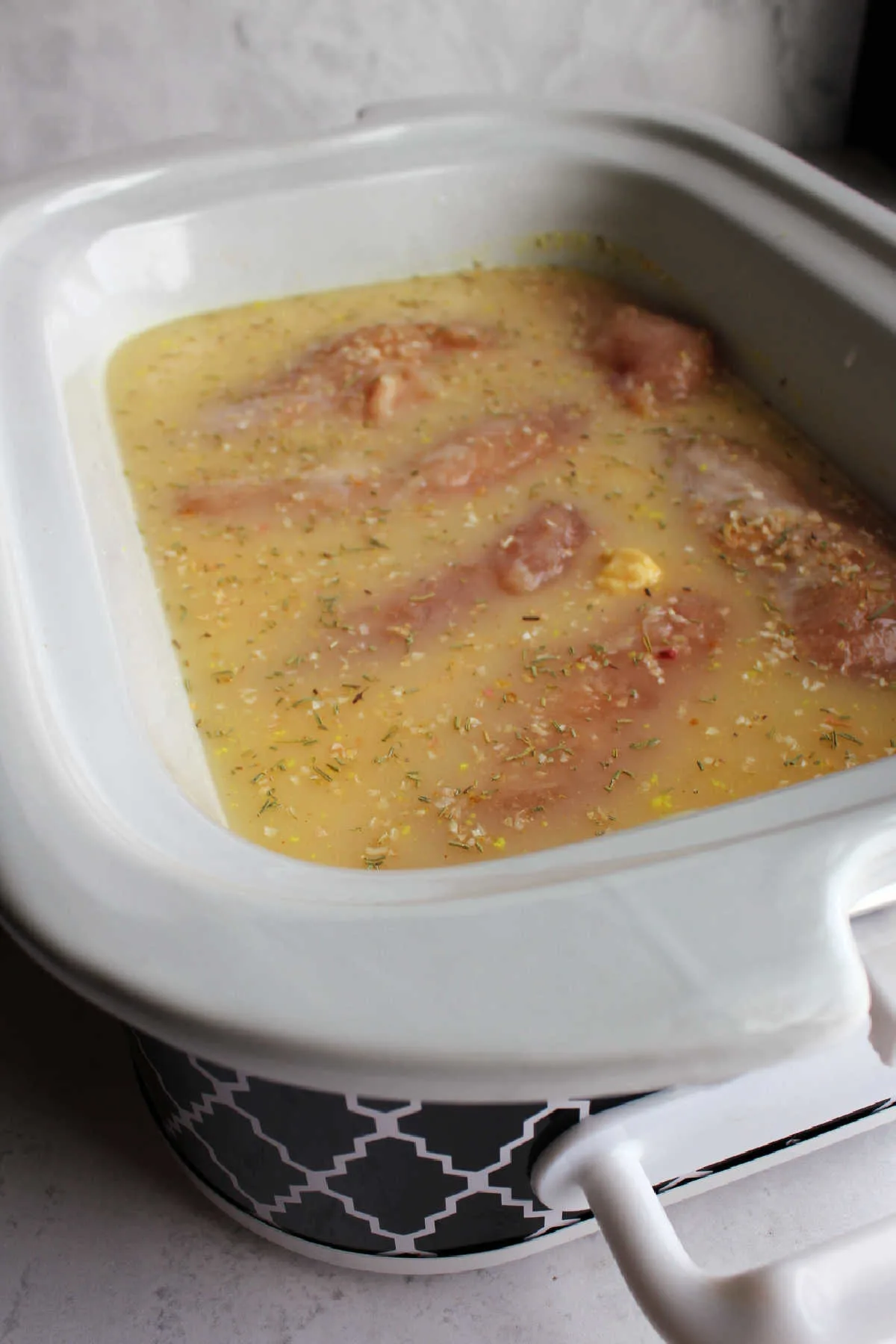 raw chicken in slow cooker with creamy gravy mixture ready to cook.