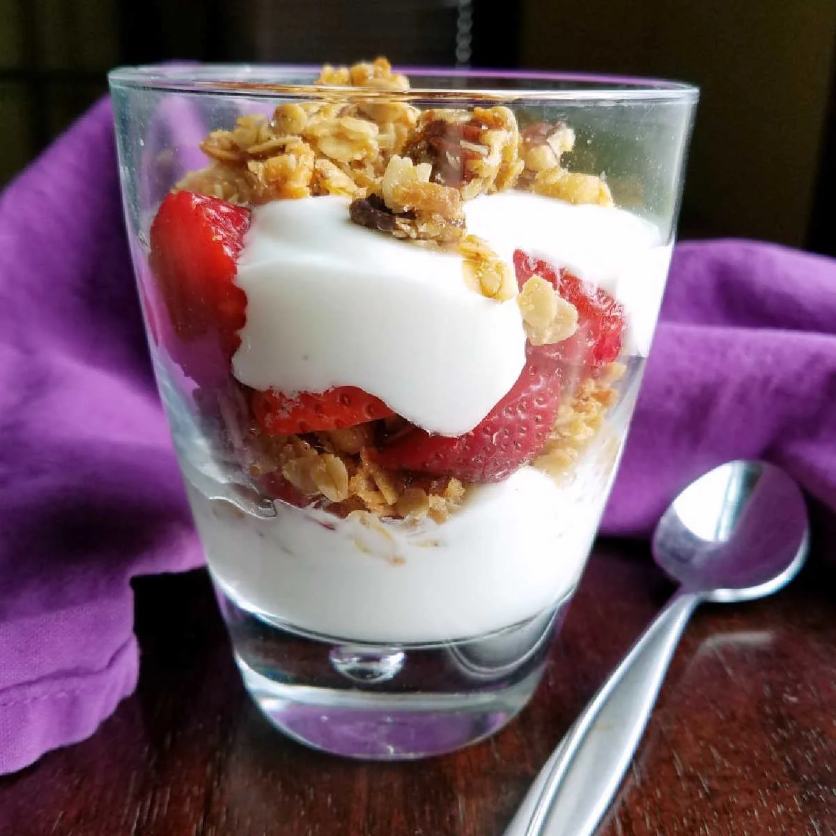 glass filled with layers of yogurt, granola and strawberries.