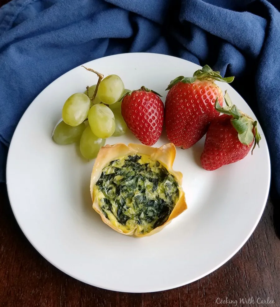 breakfast plate with two bite spinach and cheese quiche and fresh fruit.