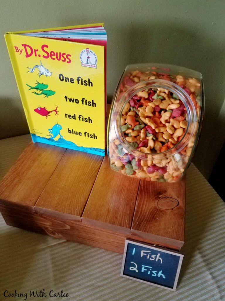 Cookie jar filled with goldfish crackers on stand next to one fish two fish book.