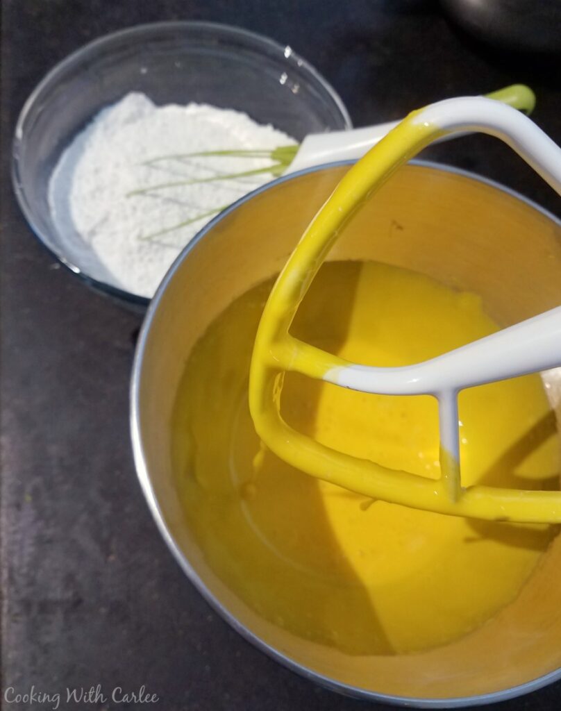 whipped egg yolks in mixer bowl with bowl of flour in background.
