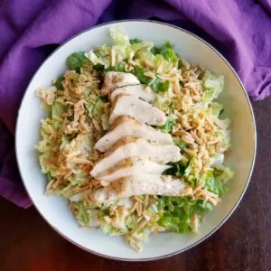Bowl of napa salad with toasted ramen and chicken breasts.