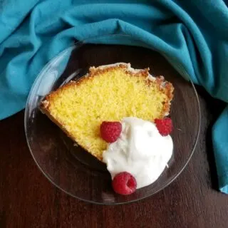 Slice of gold cake served with whipped cream and raspberries.