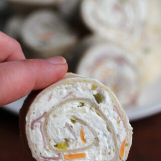 hand holding a cream cheese tortilla pinwheel appetizer with bits of cheddar cheese, beef, and pickle inside.