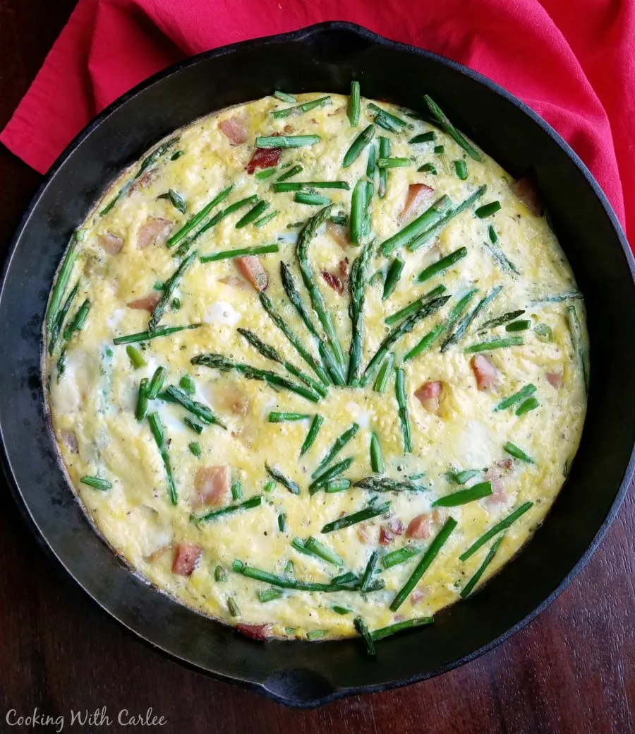 cast iron skillet full of frittata with eggs ham asparagus and cheese.