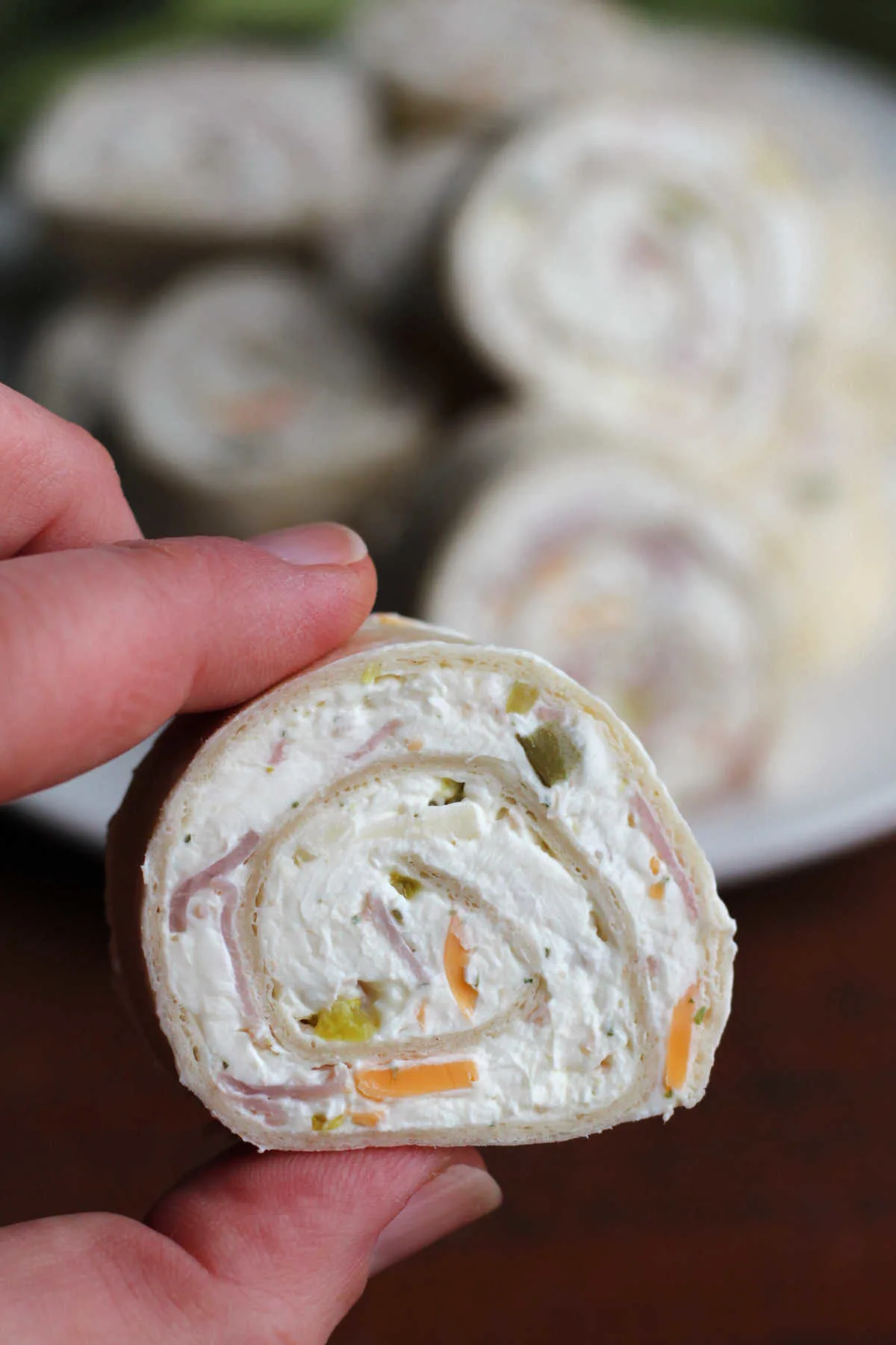 hand holding a cream cheese tortilla pinwheel appetizer with bits of cheddar cheese, beef, and pickle inside. 