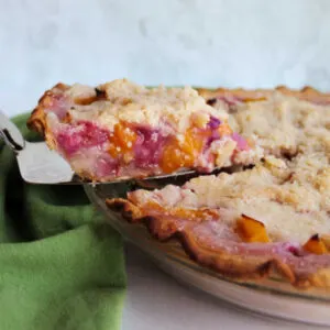 Lifting a slice of peach rhubarb pie out of pan, showing bits of fruit inside.