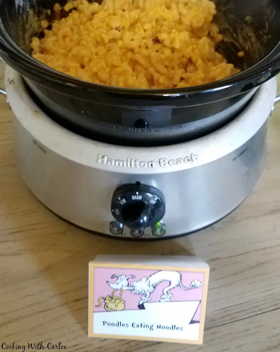 Slow cooker filled with macaroni and cheese with corn mixture with a poodles with noodles sign.