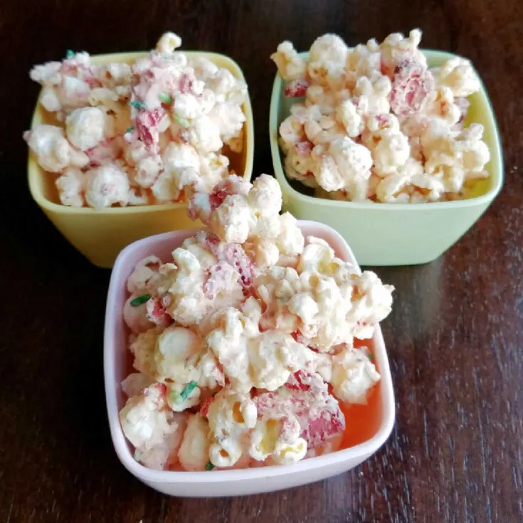 3 small bowls of white chocolate and strawberry coated popcorn.