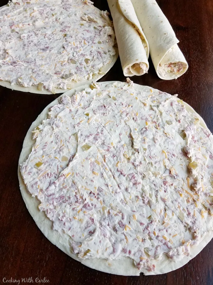 cream cheese and beef mixture spread out over large tortilla with some rolled tortillas in the back.