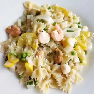 Plate of pasta primavera with shrimp, scallops, peas, squash, and more in a light creamy sauce.