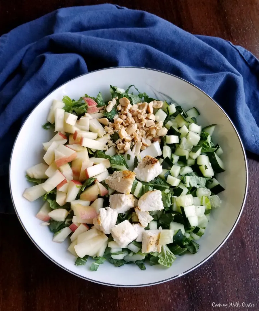 bowl full of chopped bok choy with chopped apples, cucumbers and chicken.