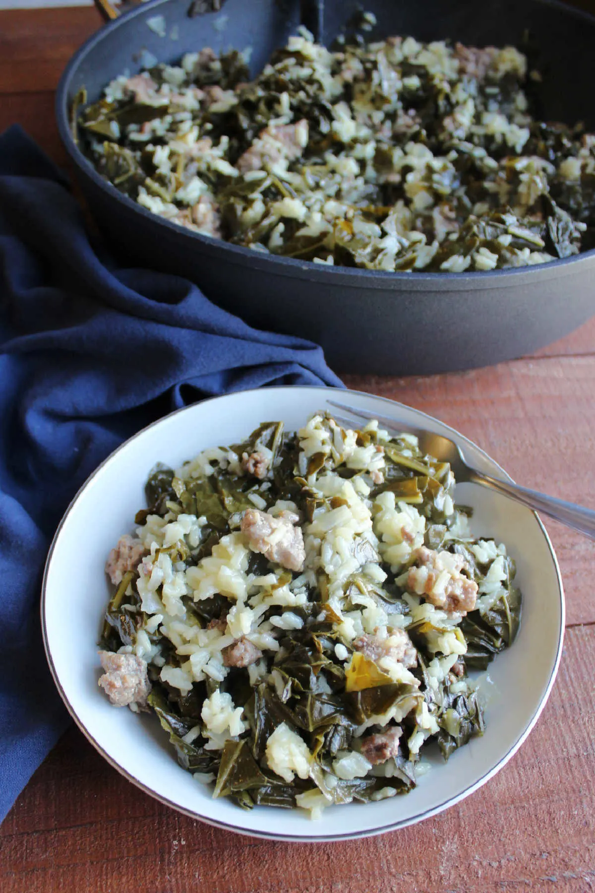 Serving of collards and rice with sausage in front of saute pan with the rest of the recipe in it. 