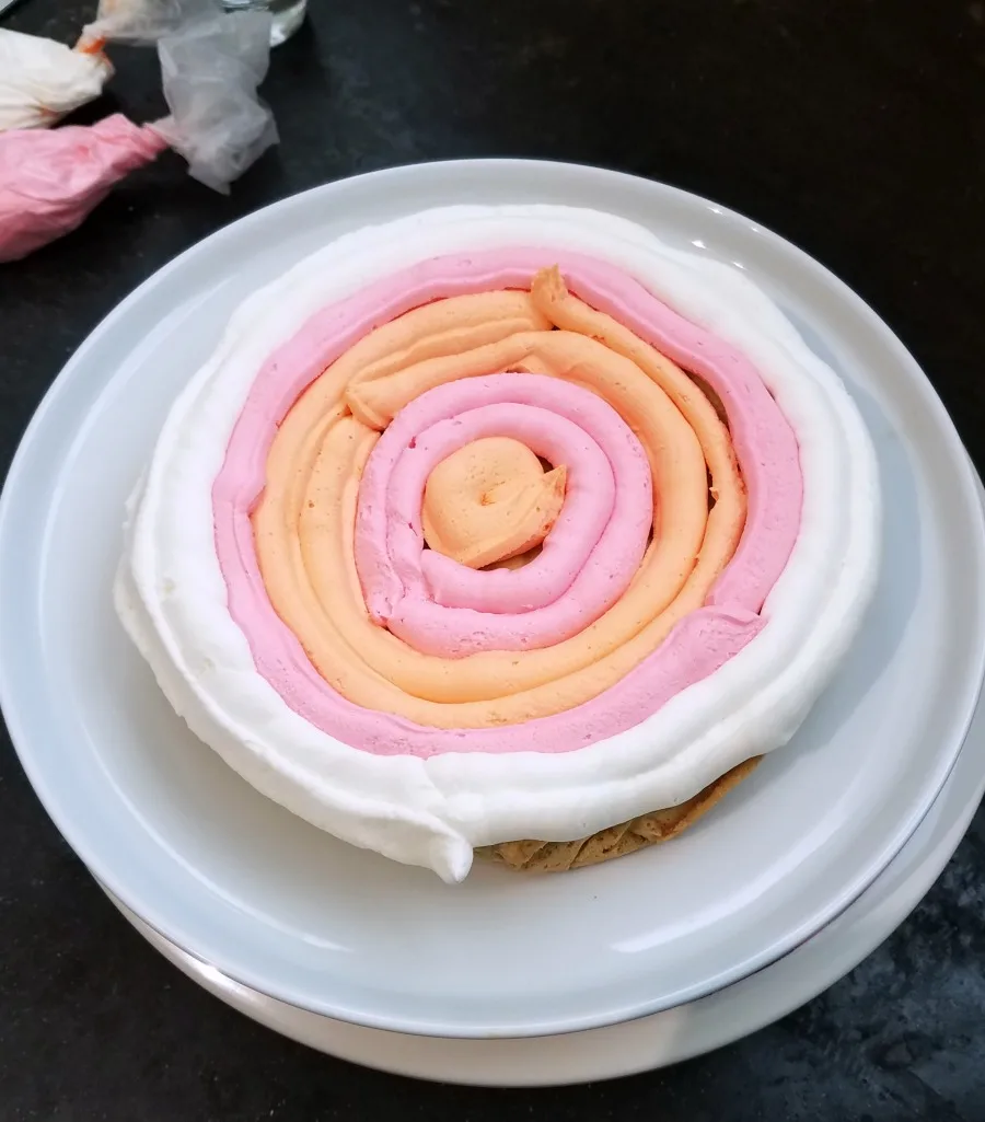 circles of pink, orange and white frosting piped onto large cookie.