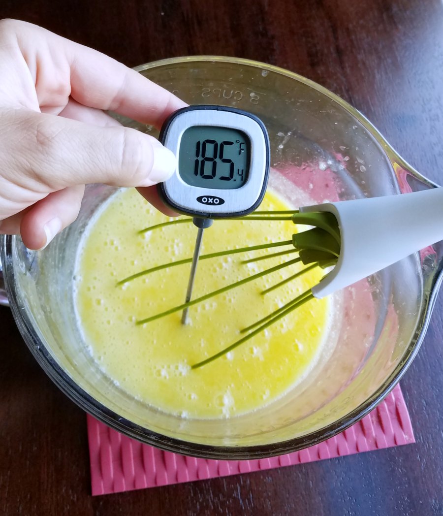hand holding instant thermometer reading 185F in bowl of lemon curd.