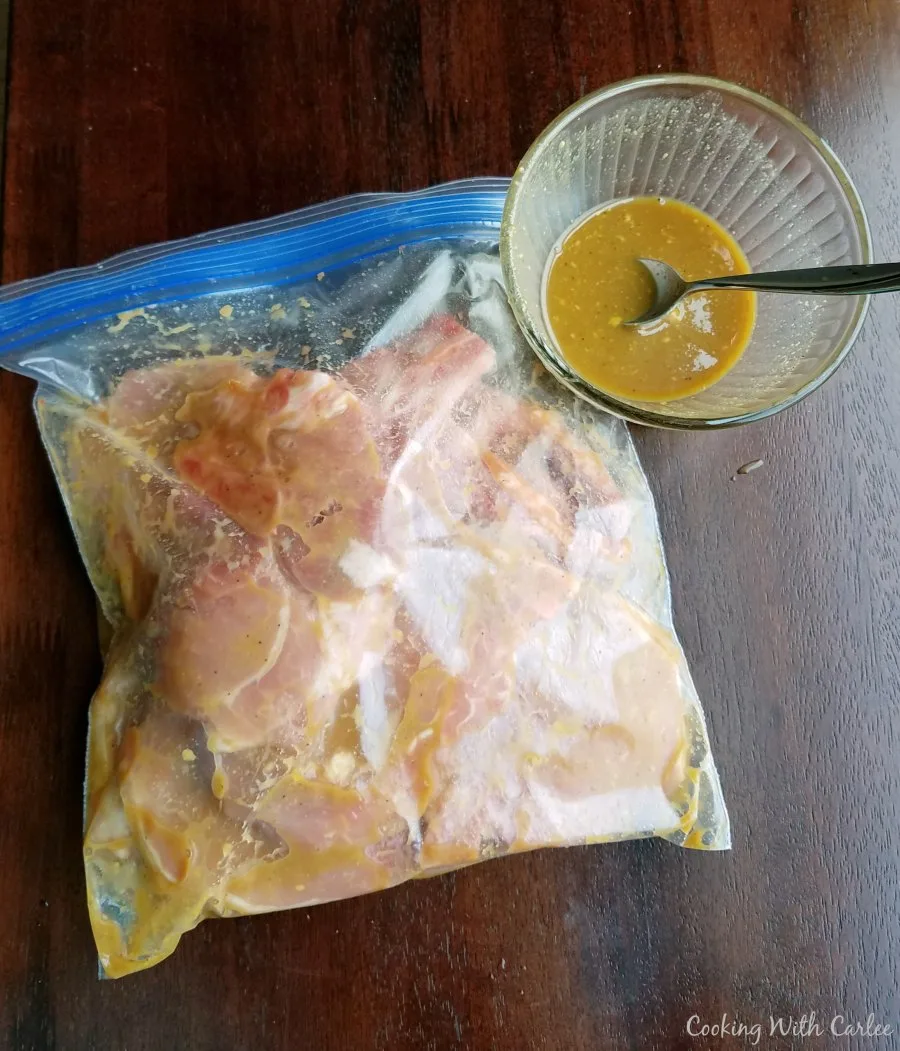 bag of marinating pork chops with a little extra marinade in a bowl nearby.