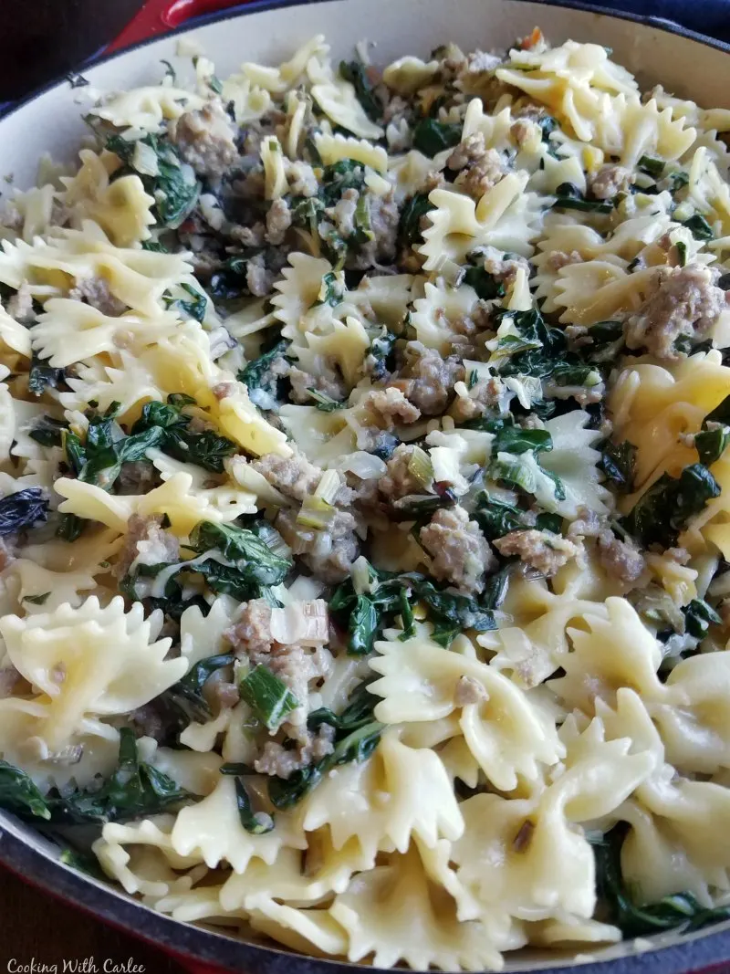 pot of creamy bowtie pasta with wilted greens and Italian sausage.