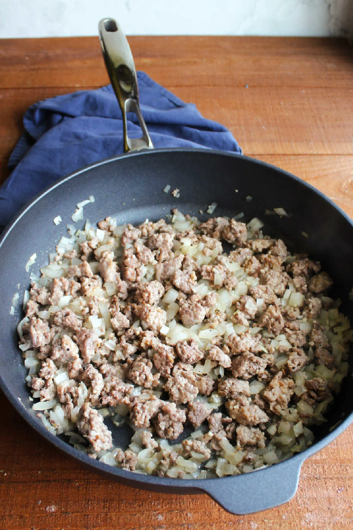 Large saute pan filled with browned sausage and translucent chopped onions, ready for the greens.
