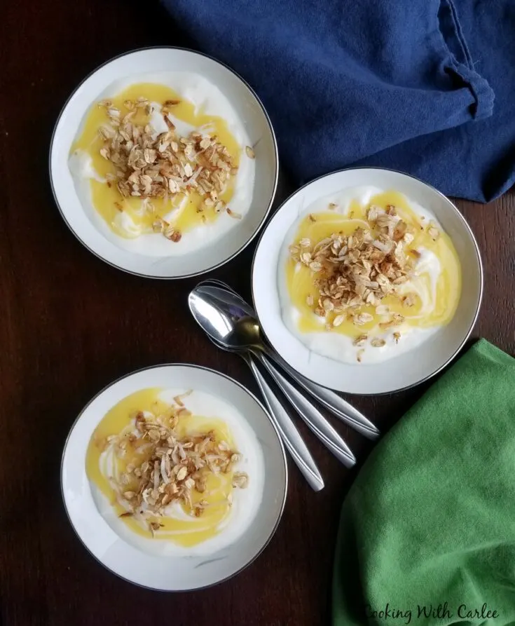 Bowls of vanilla yogurt with lemon curd and granola on top, ready to eat.