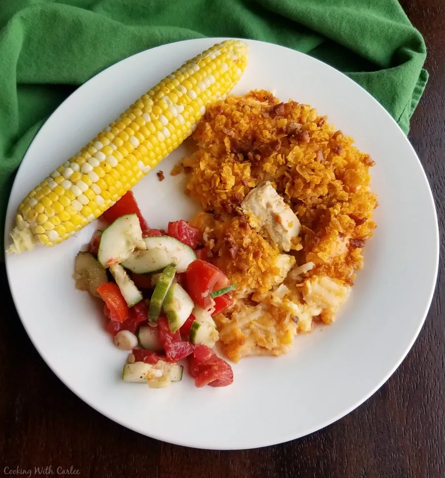 dinner plate with buffalo chicken casserole, cucumber salad and corn on the cob.