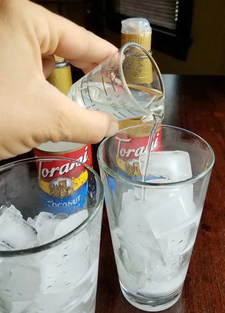 tall glasses of ice with hand pouring clear liquid overtop