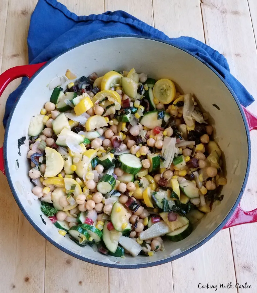 Dutch oven filled with a mix of zucchini, greens, corn and chickpeas to make a succotash style summer vegetable medley.