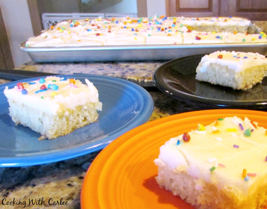Serveral pieces of white texas sheet cake with vanilla icing and sprinkles in front of pan of cake. 