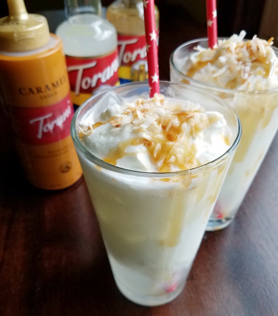 Glasses filled with coconut Italian sodas topped with toasted coconut and a drizzle of caramel sauce.