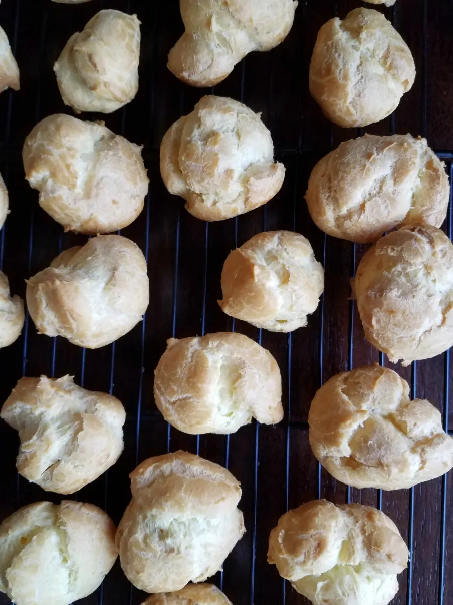 freshly baked cream puffs cooling on wire rack.