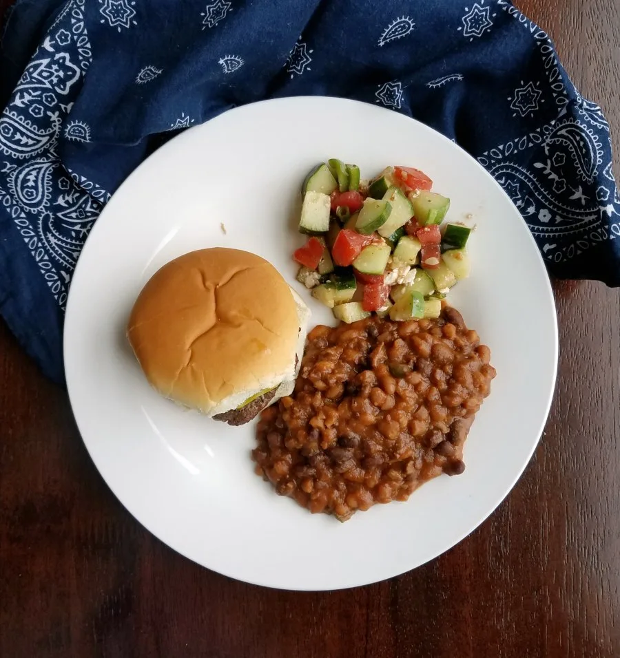 plate with burger, beans and tomato cucumber salad.