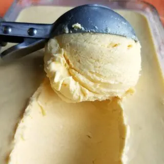 ice cream scoop dipping out a scoop of orange cheesecake ice cream.