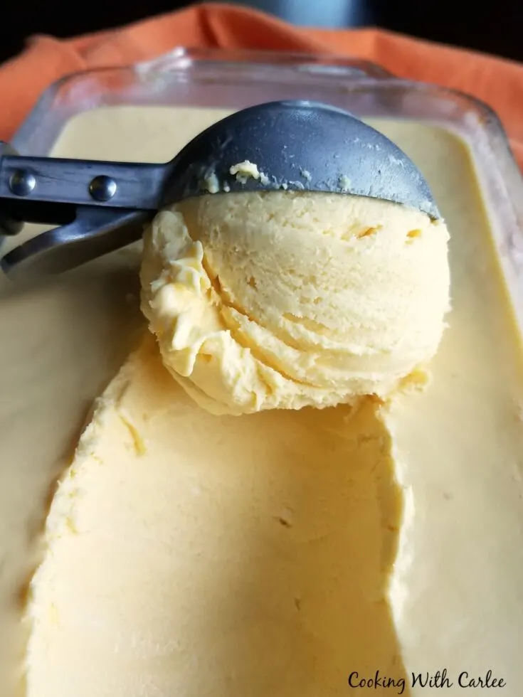 ice cream scoop dipping out a scoop of orange cheesecake ice cream.