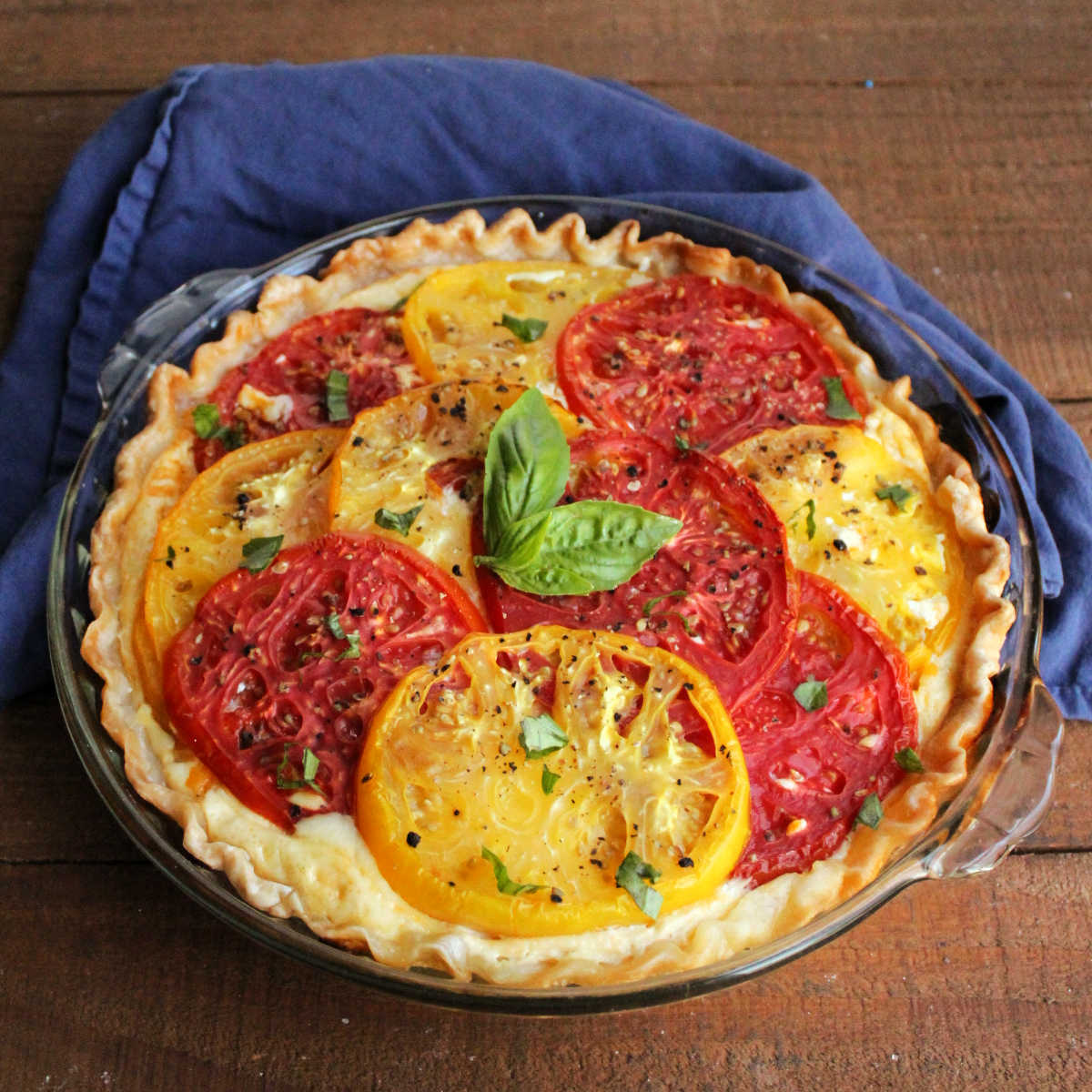 Tomato pie with slices of yellow and red tomatoes topped with fresh black pepper and bits of fresh basil.