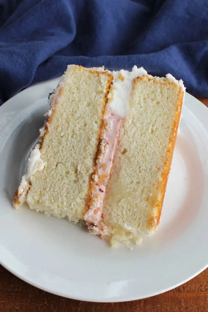 Slice of bakery style white cake with strawberry buttercream filling. 