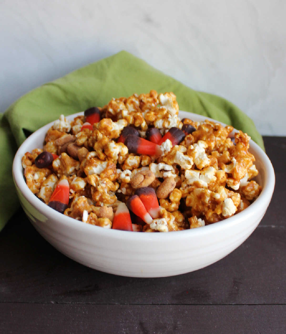 White serving bowl filled with crunchy peanut butter popcorn mixed with Indian corn candy corn and peanuts. 