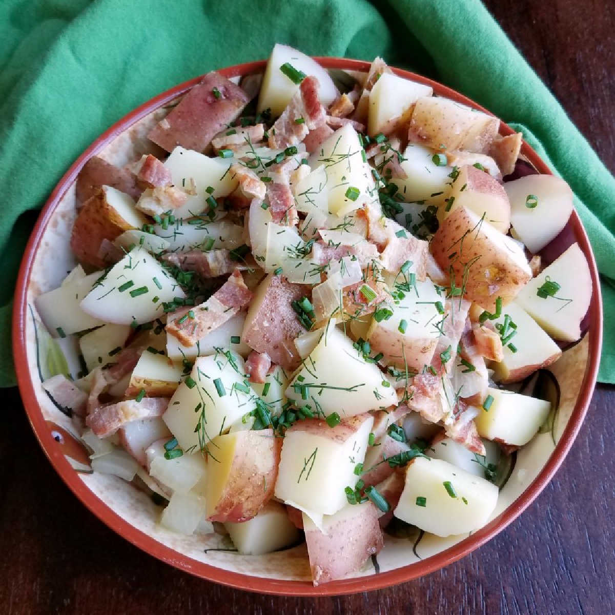 Large serving bowl filled with German potato salad with chunks of red potatoes, bacon, chives, and dill.