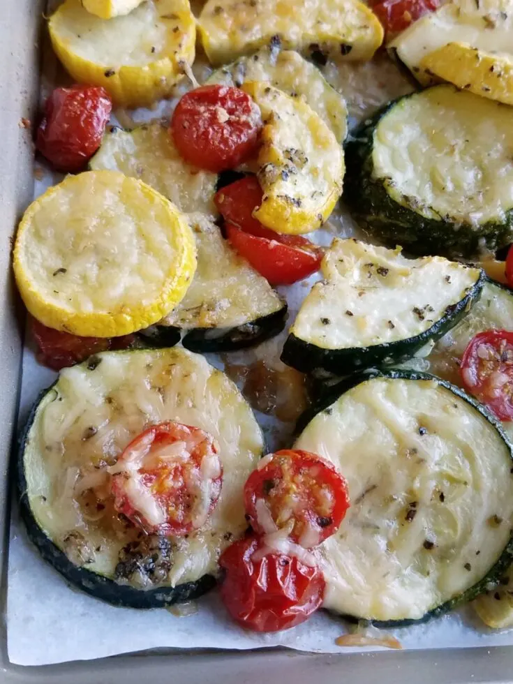 close up pan of roasted zucchini and tomatoes with melted Parmesan cheese and seasonings.