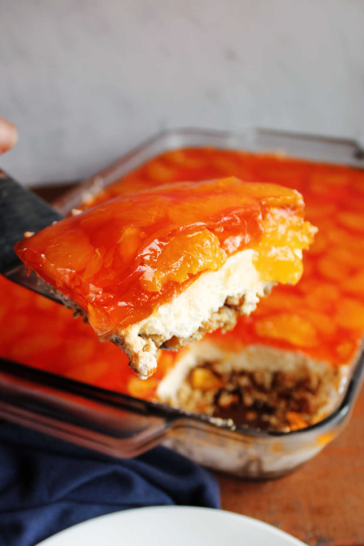 Spatula lifting piece of mandarin orange jello salad out of pan, showing layers. 
