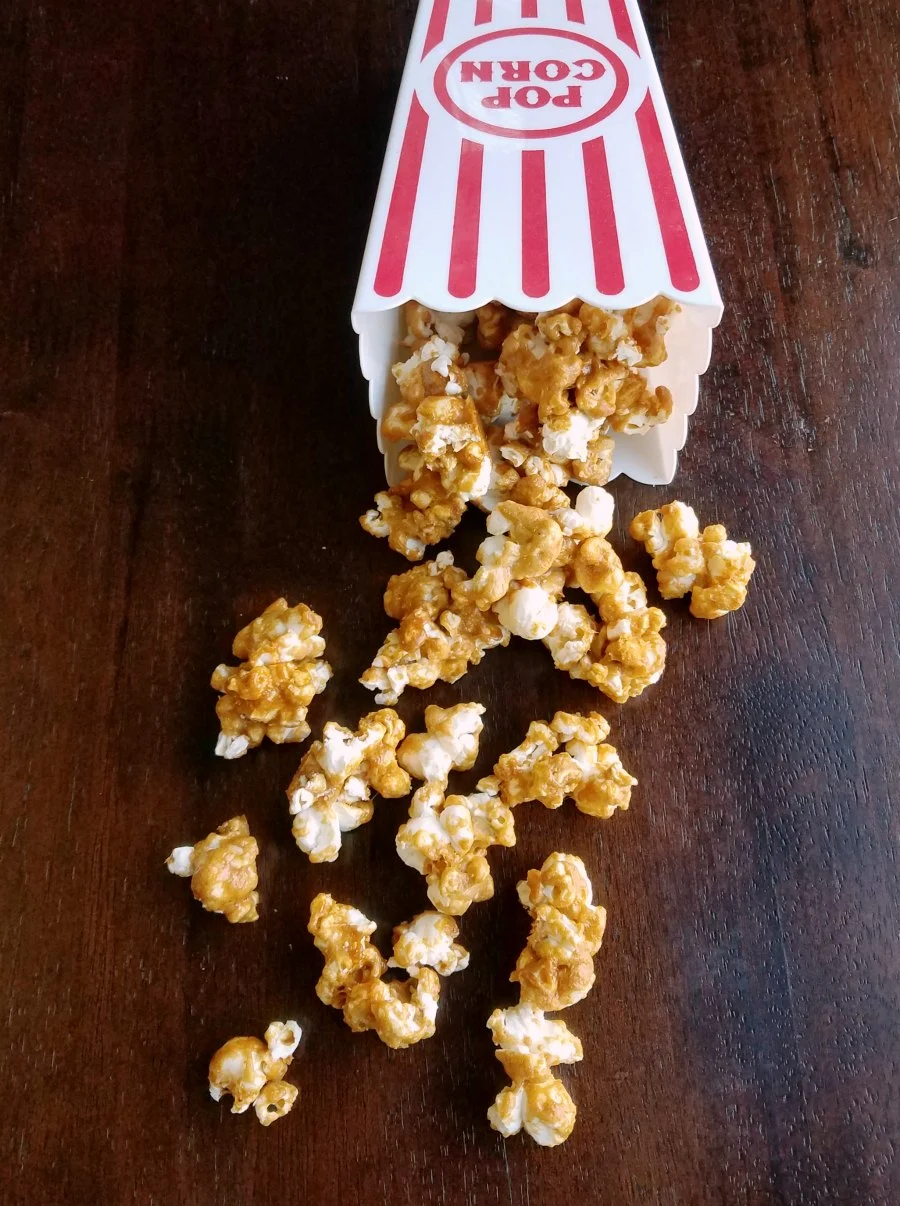 plastic popcorn tub knocked over, spilling out crunchy peanut butter popcorn. 