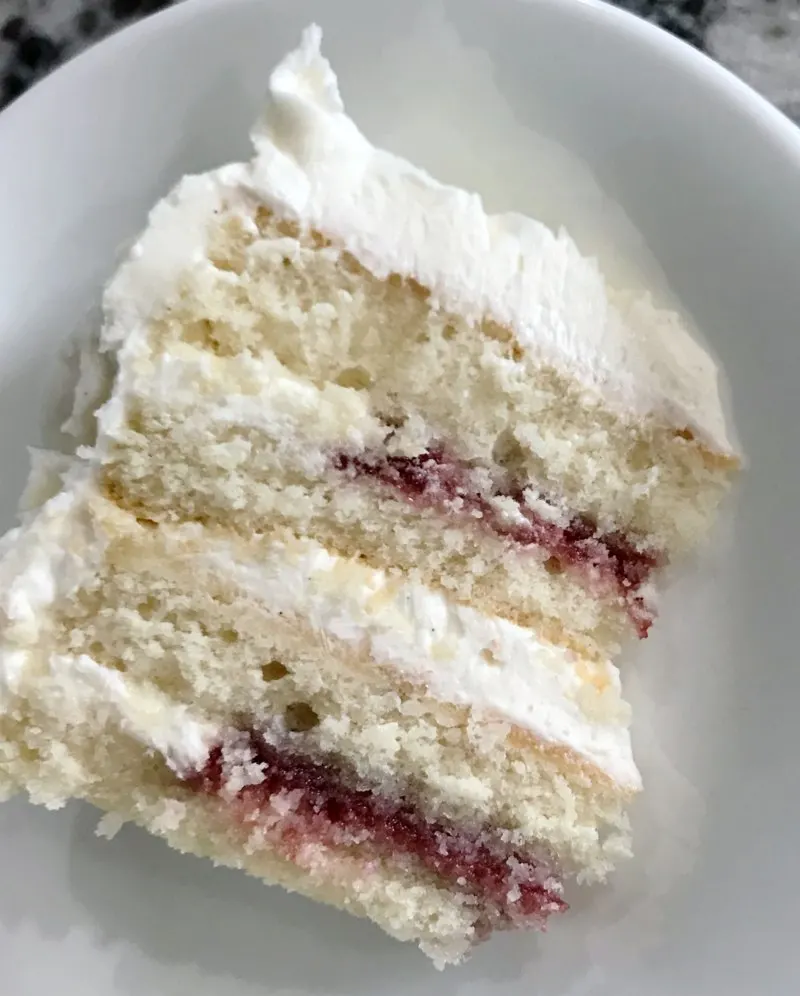 slice of cake with 4 layers of white cake, white frosting and raspberry filling.