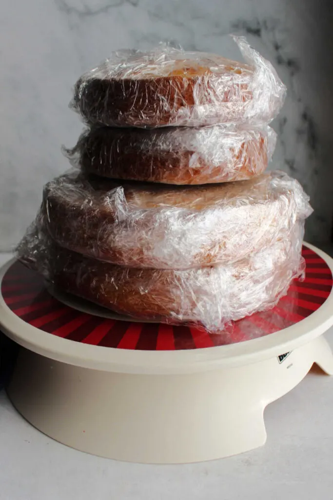 Stack of saran wrapped cake layers ready to be decorated and assembled into tiered cake.