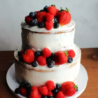 Tiered semi-naked wedding cake decorated with strawberries, raspberries and blueberries.
