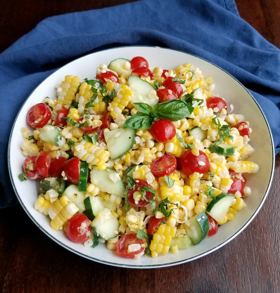 Serving bowl filled with salad made with fresh sweet corn, cucumbers, cherry tomatoes, and basil.