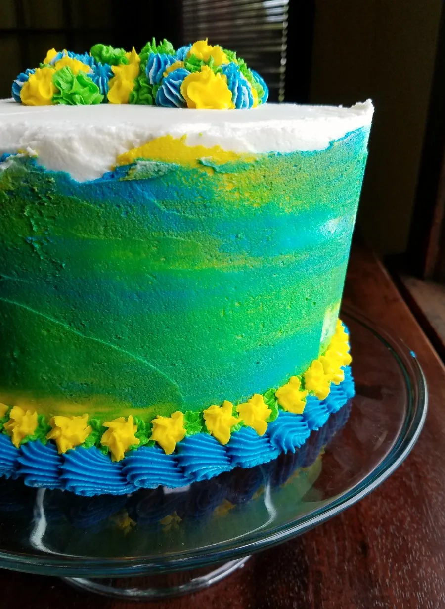 tall layered cake with blue green and yellow watercolor decoration on the outside and piped border around the bottom