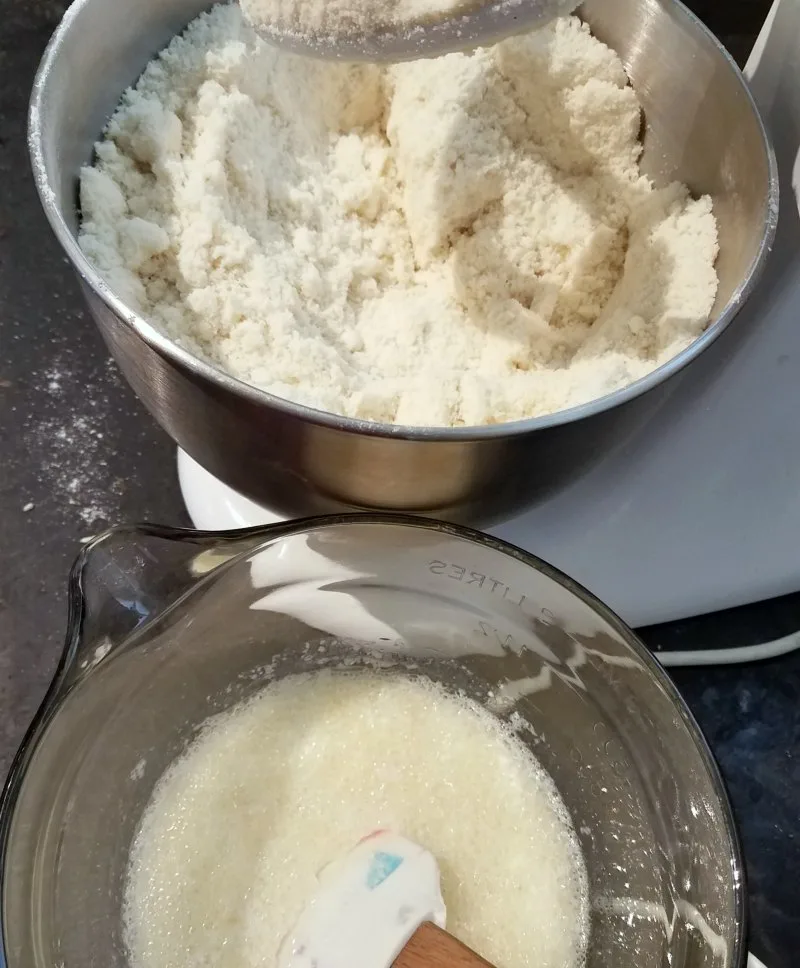 mixer full of dry ingredients with bowl of we ingredients for bakery style white cake.