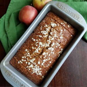 sliced loaf of applesauce oatmeal quick bread back in loaf pan with apples.