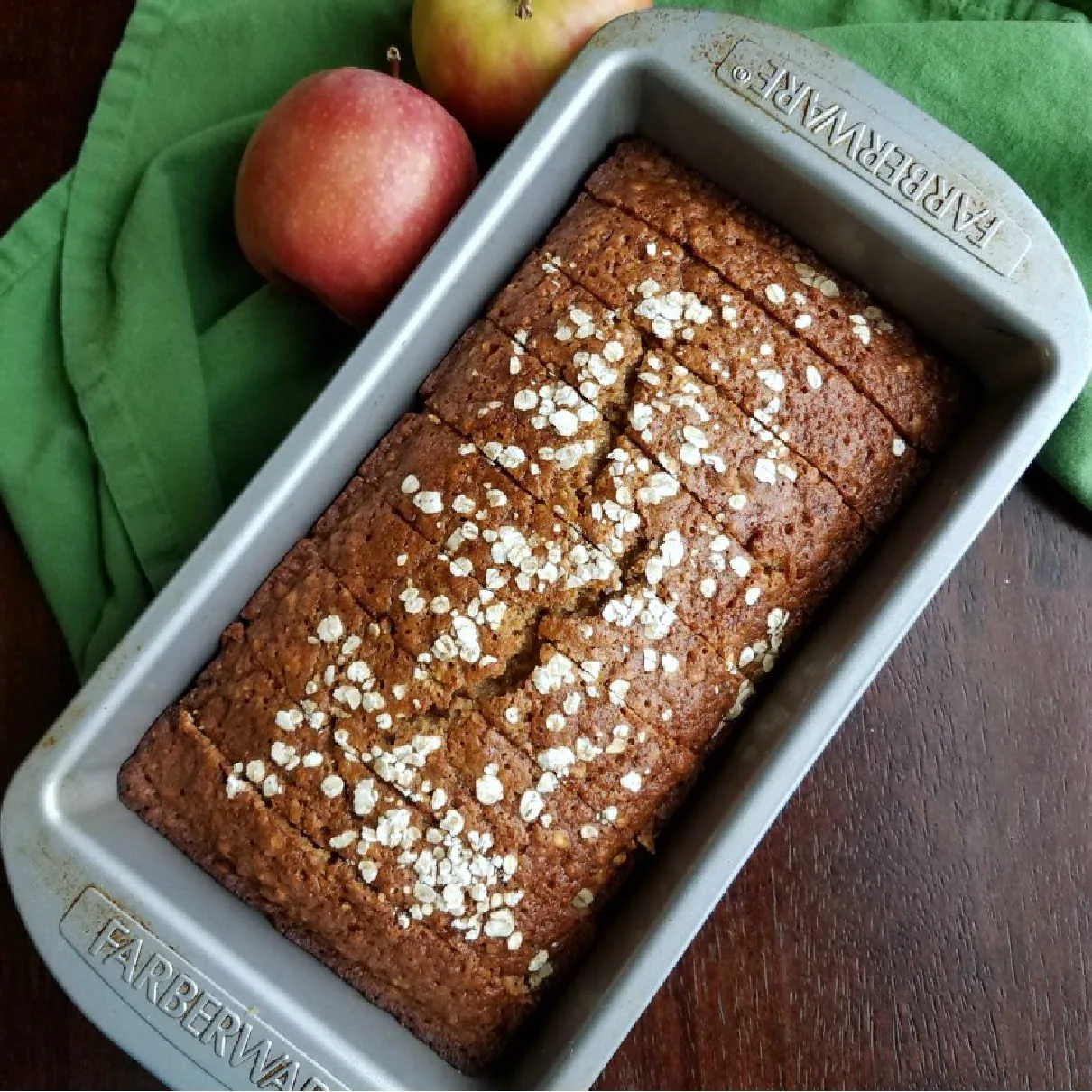 sliced loaf of applesauce oatmeal quick bread back in loaf pan with apples.